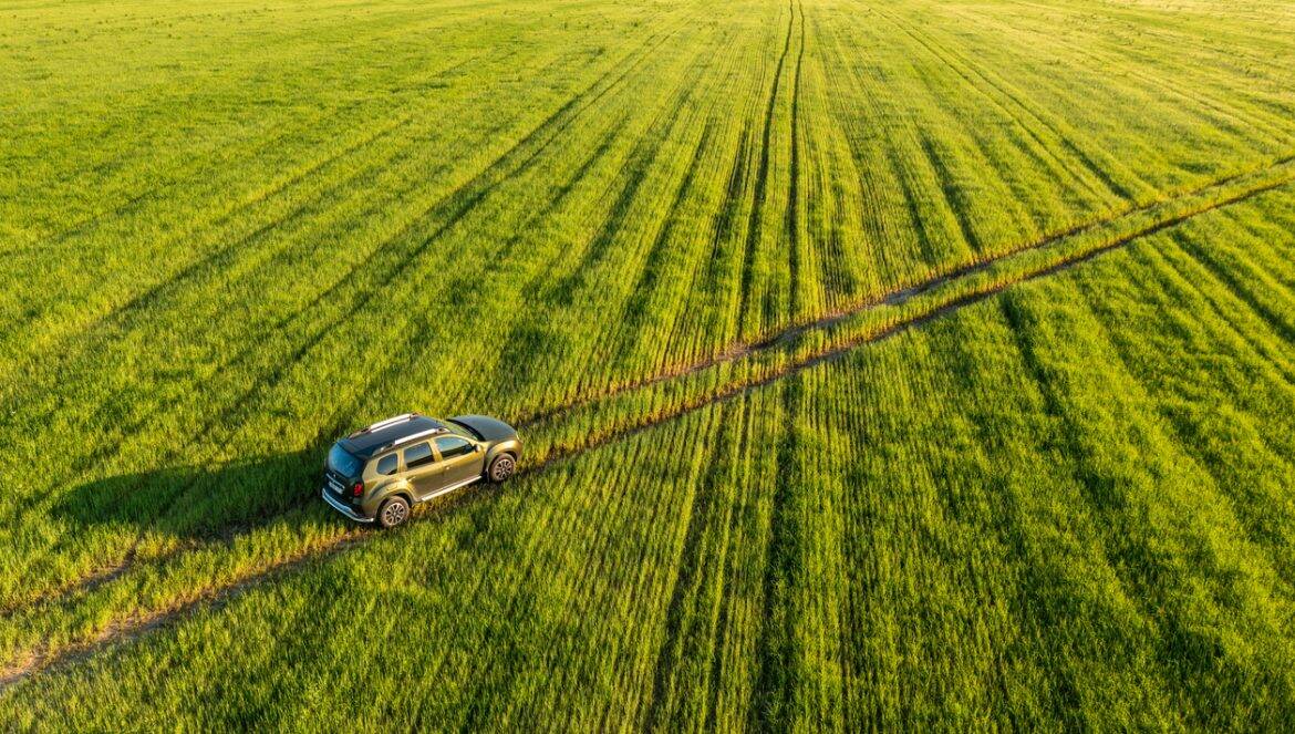 Gomel, Belarus - June 17, 2021: Aerial view of Renault Duster car suv mooving on countryside road in spring field rural landscape. Renault Duster or Dacia Duster Suv in road through summer green corn field in sunny evening. Car drives through corn maize plantation.