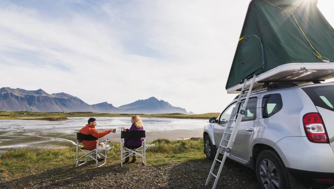 Hofn, Iceland - August 2018: Young couple sitting in folding chairs next to offroad car with tent on the roof.