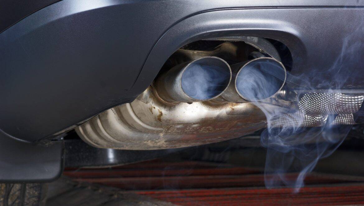 Exhaust pipe of a car - blowing out the pollution. Exhaust pipe coming out of the car with its exhaust. View from below, see the bottom of the exhaust pipe silver. Visible rear bumper eclipse of gray.