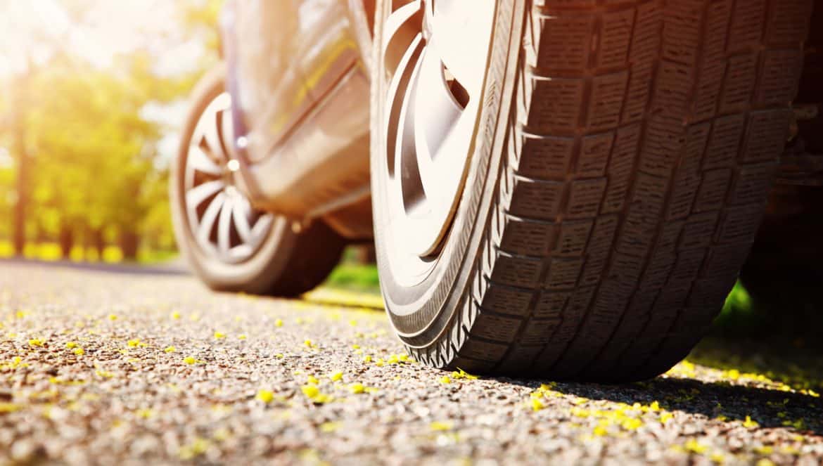 Car tires closeup on asphalt road on summer day at park. Vehicle outdoors in nature with beautiful sunlight. Transportation, vacations and travel conceptCar on asphalt road on summer day at park
