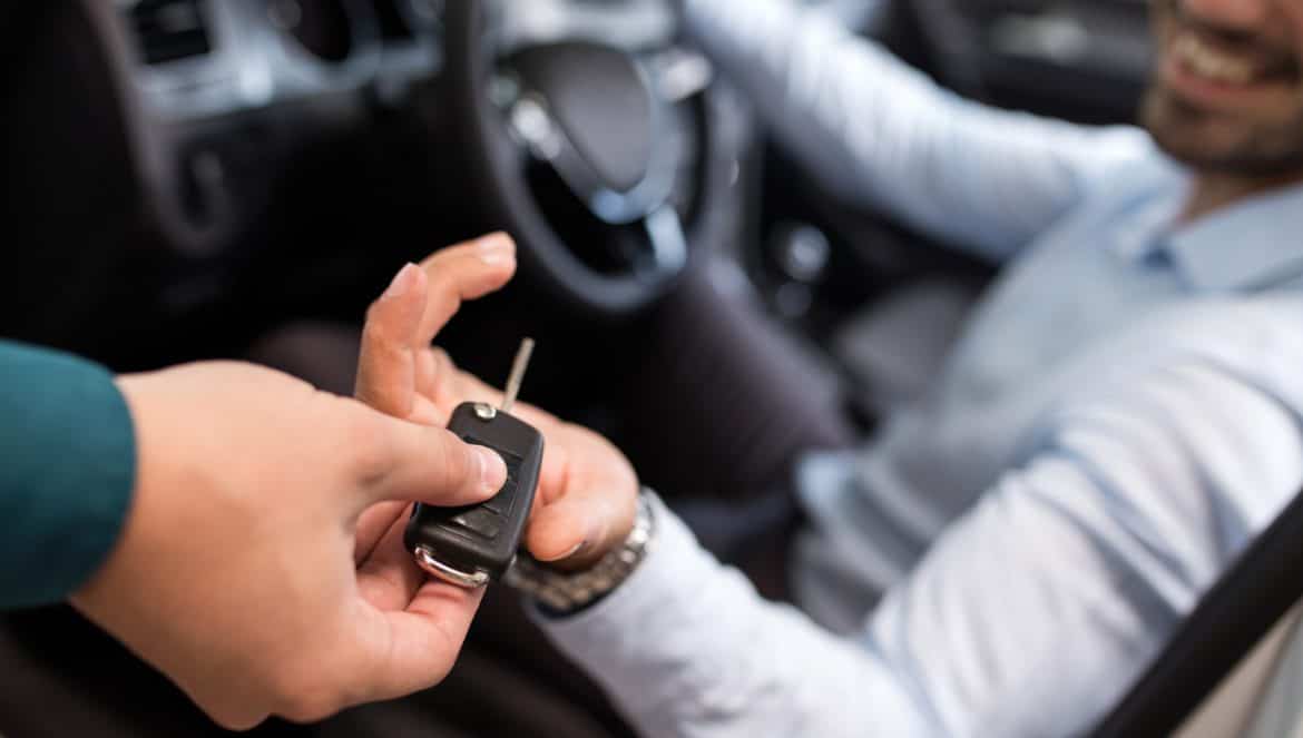 Close up of a man sitting in a car and receiving car keys from unrecognizable person.
