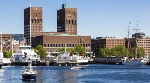 A sail boat sails from the marina in the Oslo fjord in front of the City hall building in Norway capital city on a sunny day.