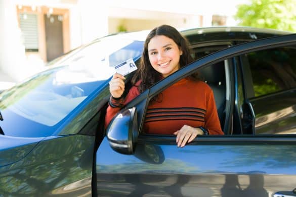 Portrait of a cheerful teen girl showing her driving license while sitting in her new car