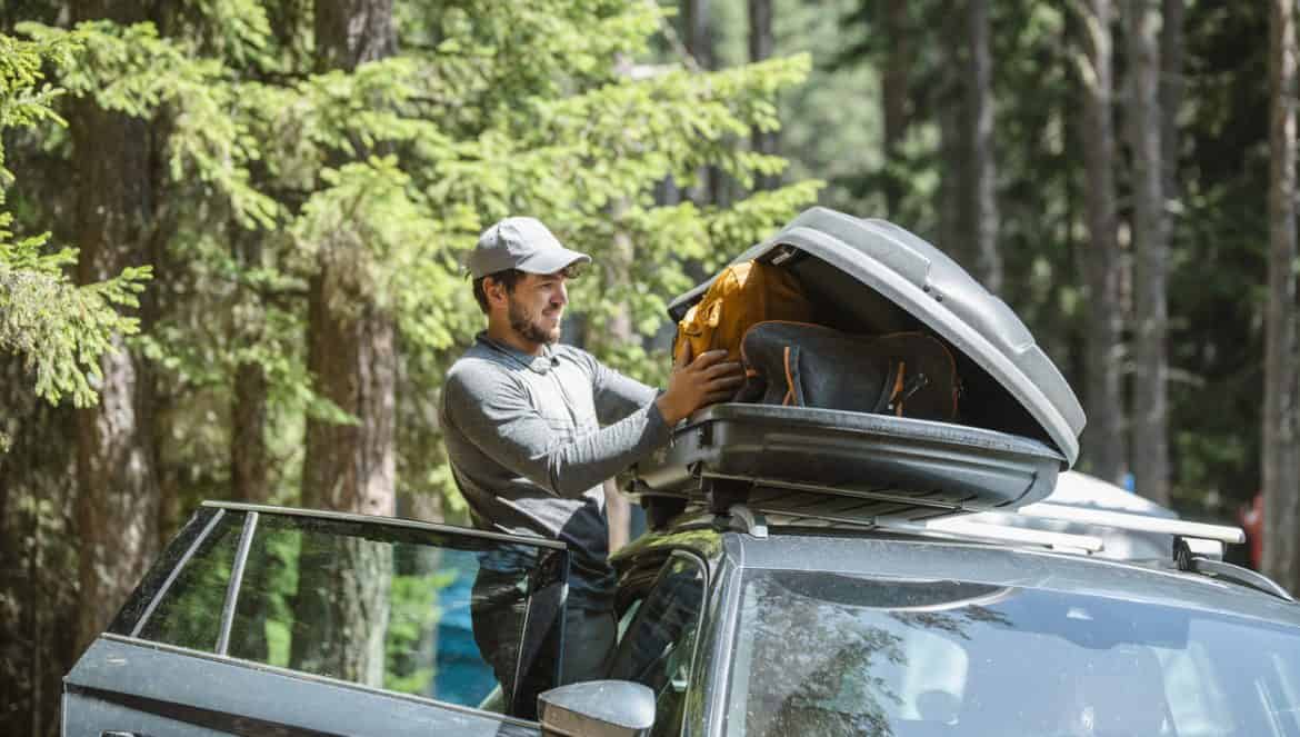 Mid adult man filling cargo box container on roof rack for camping vacation.