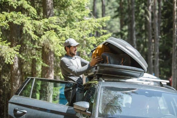 Mid adult man filling cargo box container on roof rack for camping vacation.
