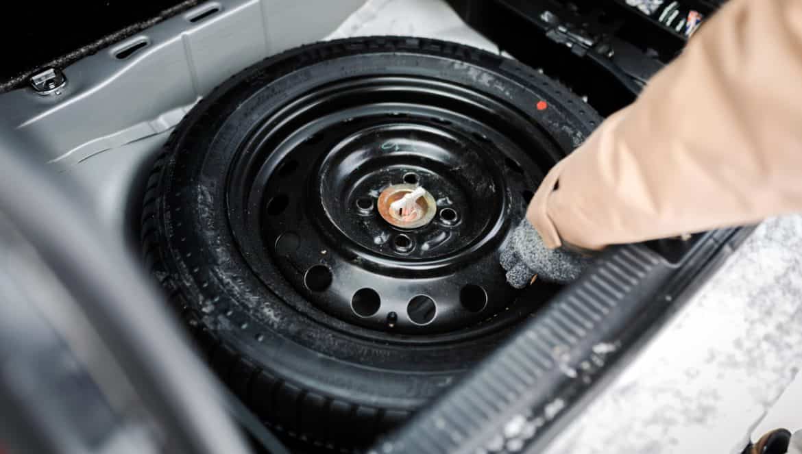 Driver changing spare tyre after accident. Broken and flat car wheel after crash.