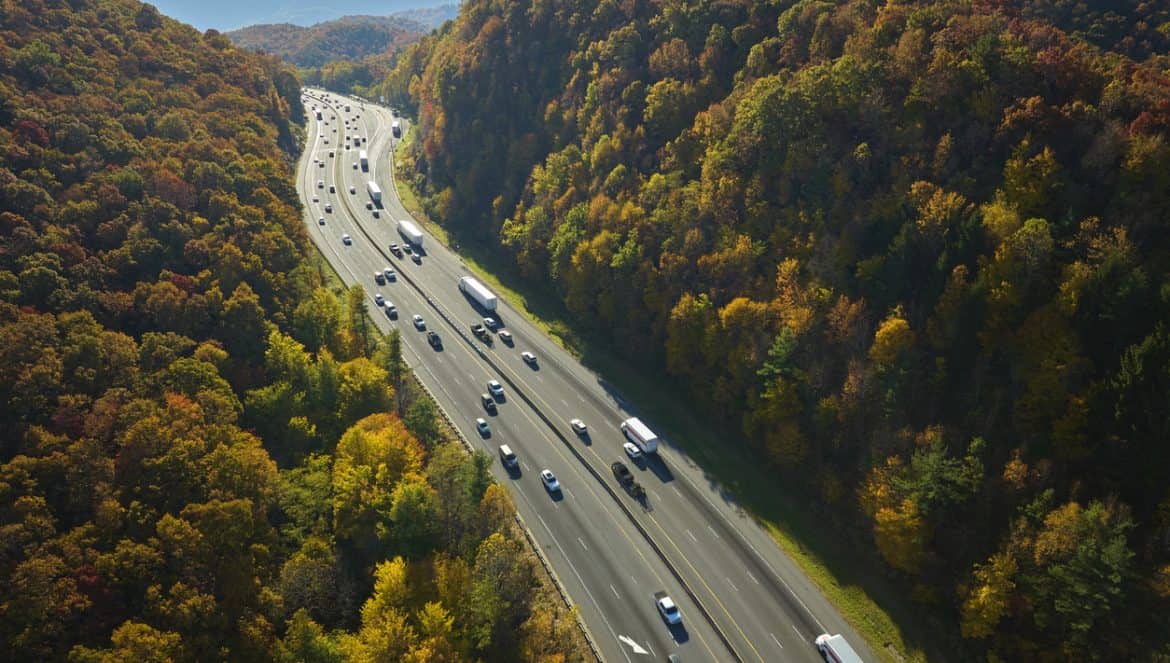 Aerial view of I-40 freeway in North Carolina heading to Asheville through Appalachian mountains in golden fall with moving trucks and cars. Interstate transportation concept.